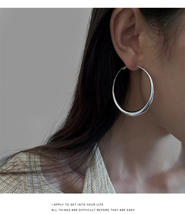 Détail macro de grandes créoles géométriques en argent poli sur un mannequin