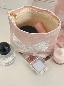 Detail of pink satin makeup bag featuring white embroidered bow and pearl zipper pull