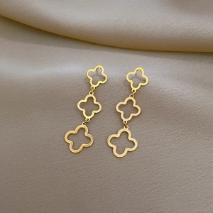 Detailed view of golden triple hollow-out clover tassel earrings on soft fabric