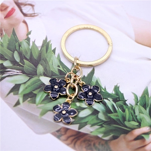 Close-up of golden keychain with three dark blue enamel flower pendants on a lifestyle background