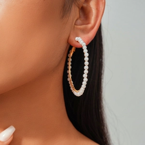 Close-up of a large gold hoop earring with white pearls worn by a female model
