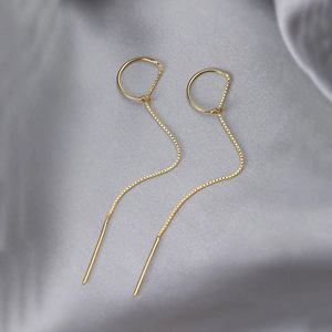 Minimalist long gold chain earrings with geometric circle charms on grey silk background