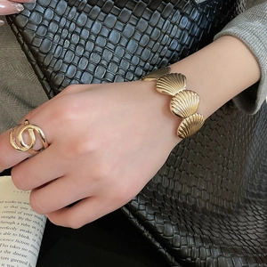 Close-up of golden wrinkled starfish shell bracelet and interlocking ring on female wrist