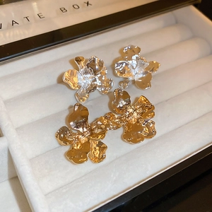 Detailed close-up of gold and silver irregular metallic flower earrings with wrinkled texture
