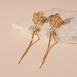 Detail of elegant gold tassel earrings with zircon hollow flowers on white stone