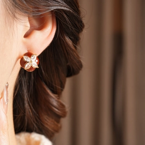 Close-up of diamond flower stud earring with red enamel petals on model's ear