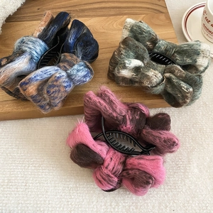 Detail of plush faux shearling bow hair clips in mixed colors on a wooden tray
