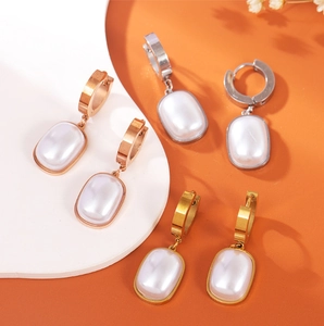Macro detail of gold and silver hoop earrings with oval pearl charms on a modern tray