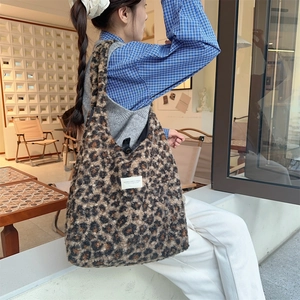 Detailed view of large leopard print plush tote bag worn by a model in a cozy cafe setting
