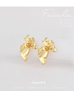 Detail shot of golden flower earrings with textured petals on a white pedestal