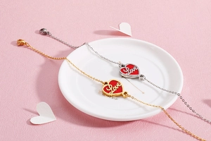 Detail of gold and silver heart bracelets with red Love enamel pendants on a white plate