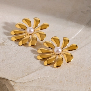 Detail shot of gold-plated daisy flower earrings with white pearl centers on stone