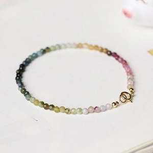 Minimalist 2mm gradient tourmaline beaded bracelet with golden clasp on artistic background