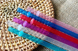 Dettaglio di sei cannucce colorate riutilizzabili in plastica con glitter su base in rattan