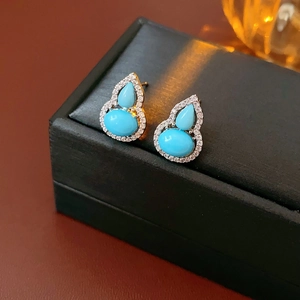 Detail of turquoise gourd earrings with gold plating and crystals on a black jewelry box