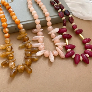 Close-up of resin beaded necklaces in amber, pink and burgundy with gold hardware