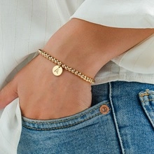 Détail d'un bracelet à perles dorées avec pendentif lettre A sur le poignet