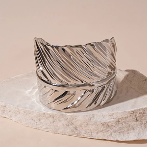 Macro detail of silver open bangle featuring intricate engraved feather leaf textures