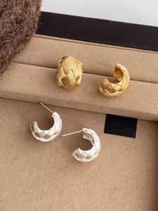 Macro detail of gold and silver C-shaped earrings with woven texture on a velvet tray