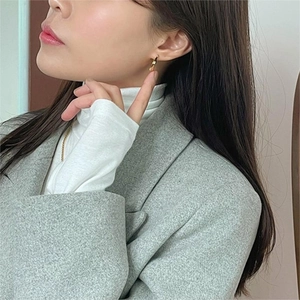Close-up of a small polished golden hoop earring worn by a model in a grey blazer