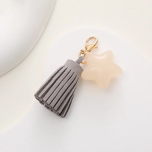 Close-up of grey suede tassel and beige star pendant keychain with gold clasp detail