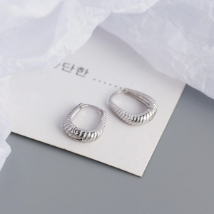 Macro shot of silver twisted hoop earrings with fine ribbed texture on a white background