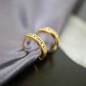 Nahaufnahme goldener Creolen mit hohlen römischen Ziffern auf Satin-Hintergrund