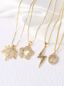 Detail of four gold-plated pendant necklaces with cross, bolt, and leaf designs on silk