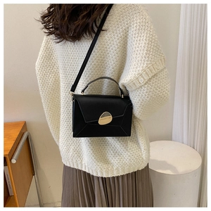 Detail of black leather crossbody bag with unique gold hardware worn by a model
