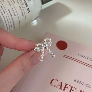 Close-up of a silver bow ring with beaded elastic band next to a perfume bottle