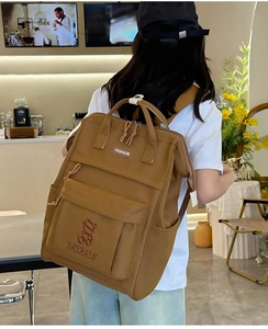 Brown nylon backpack with fashion bear embroidery worn by a model in a cafe setting