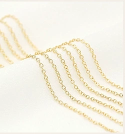 Macro shot of fine gold necklace chain links on white fabric showing metallic texture