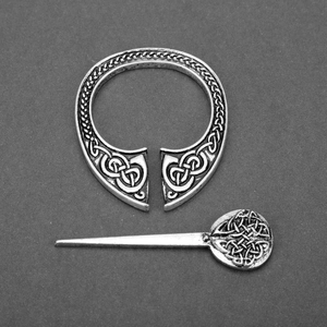 Detail of silver Viking cloak pin showing intricate Celtic knot patterns on metal