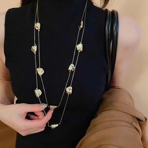 Dettaglio di una collana lunga dorata a strati con ciondoli geometrici irregolari