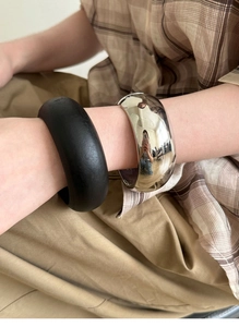 Close-up of wide minimalist bracelets in matte black and polished silver finish
