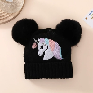 Detail of black knit hat featuring colorful unicorn embroidery and double faux fur pom-poms