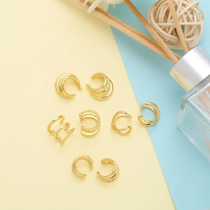 Flat lay of multiple gold geometric irregular ear cuffs on a pastel dual-tone background