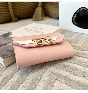Détail d'un portefeuille rose avec boucle noeud dorée et texture cuir grainé