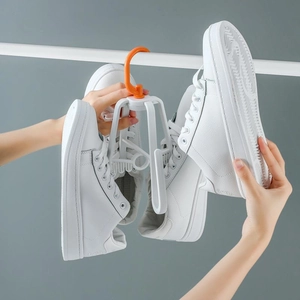 Rotating white shoe drying rack with orange hooks holding a pair of white sneakers