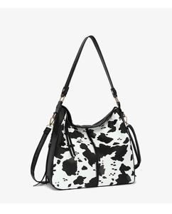 Close-up of cow print PU leather crossbody bag with gold hardware and black straps