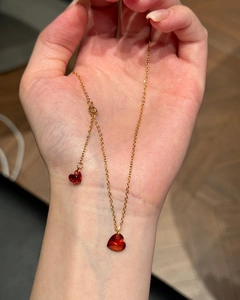 Detail of gold heart necklace with vibrant red crystal pendant held in hand