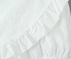 Detailed close-up of white floral eyelet embroidery fabric with ruffled edge design