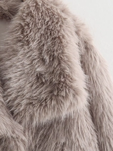 Close-up detail of luxurious faux fur collar and taupe textured fibers on woman jacket