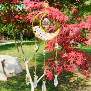 Detail of moon suncatcher with pink crystal stones and hanging prisms on red leaves