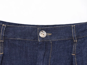 Vista macro dettagliata della vita in denim blu scuro con bottone argento e cuciture gialle