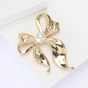 Elegant gold bow brooch with center pearl detail on a white platform for women