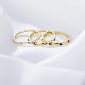 Three elegant gold rings with clear green and blue zircon stones on white fabric