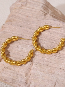 Detail of twisted 18K gold plated stainless steel hoop earrings on a stone surface
