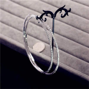 Macro detail of large silver crystal hoop earrings adorned with rhinestones on a black stand