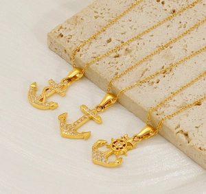 Close-up of gold-plated anchor and rudder pendants with white cubic zirconia on stone base